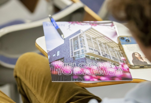 Welcome to ˿Ƶ orientation book on a desk a student is sitting at