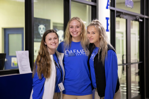 Three ˿Ƶ students in blue ˿Ƶ sweat shirts standing in hallway smiling